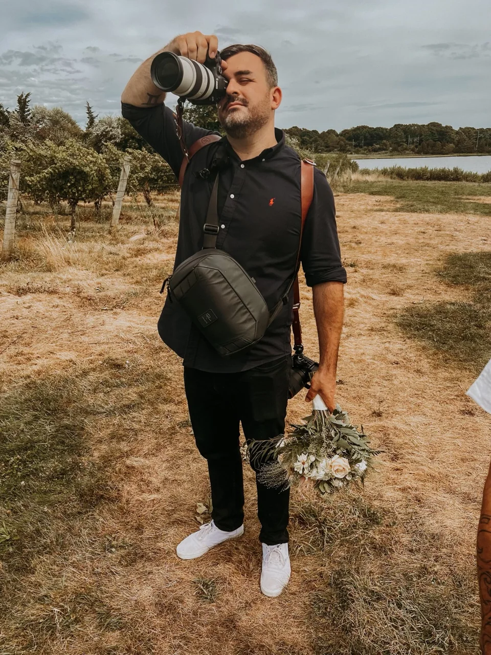Liam photographing a wedding, camera raised and bouquet in hand